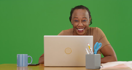 Mature black woman using laptop smiling at camera on green screen