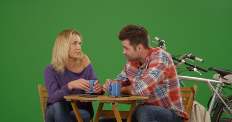 Millennial white couple sitting at cafe table drinking coffee on green screen