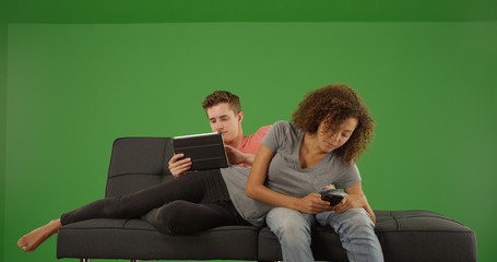 Bored couple using handheld tech devices on couch on green screen