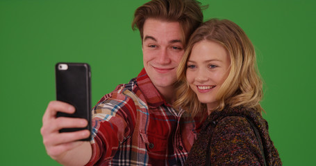 White millennial couple taking selfies with smartphone on green screen