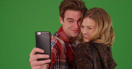 Millennial couple taking selfies with mobile device on green screen