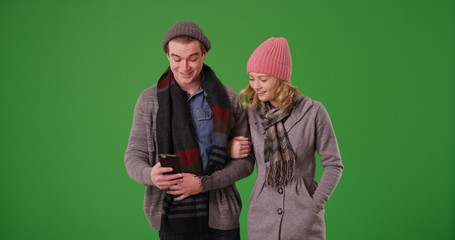 Young couple or friends in winter clothes using cellphone on green screen