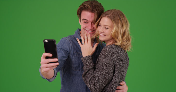 Happy engaged couple taking selfie with cellphone on green screen