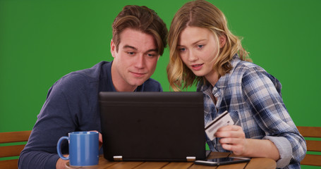 Young couple making online payments with credit card on laptop on green screen