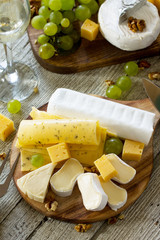 Cheese plate with grapes,  wine glass and nuts on a wooden table.