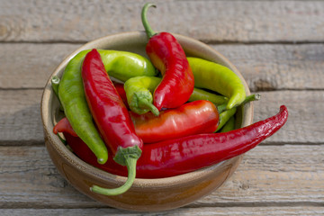 Red and green bitter, hot pepper lying in a brown ceramic plate on a wooden background