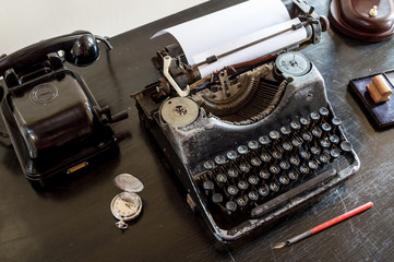 Old typewriter with a piece of paper on an old black Desk , phone, pocket round clock.