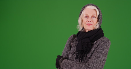 White senior female in winter clothes posing with arms crossed on green screen