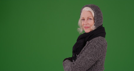 Charming elderly woman in winter attire posing with arms crossed on green screen