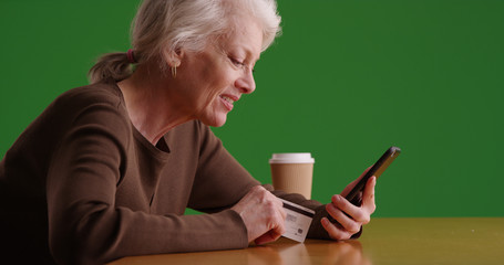 Mature white woman shopping online on phone and credit card on green screen