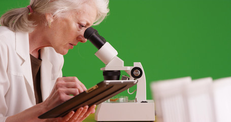 Female researcher using microscope recording data on tablet on green screen