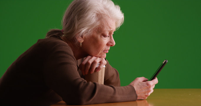 Profile of sad looking white senior woman using smartphone on green screen