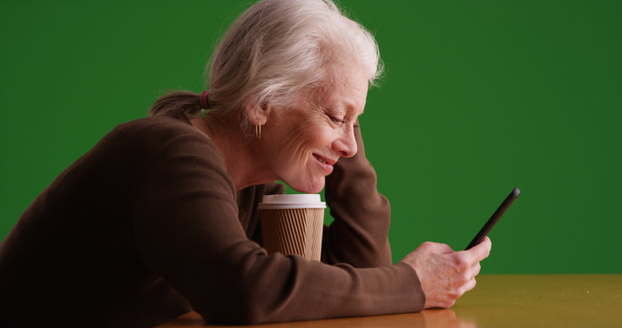 Smiling white female senior with coffee using mobile device on green screen