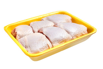Raw and uncooked chicken thighs in a yellow plastic container. Meat of poultry in tray, isolated on white background