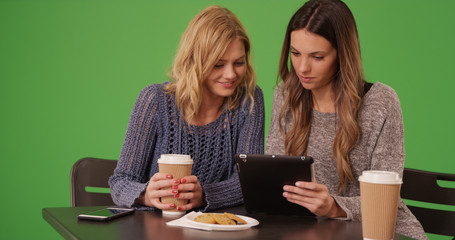 Lovely couple of girls sitting and sharing tablet computer on green screen