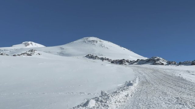Panorama of the peak of Elbrus. The teenager rises up the path and shoots the camera.