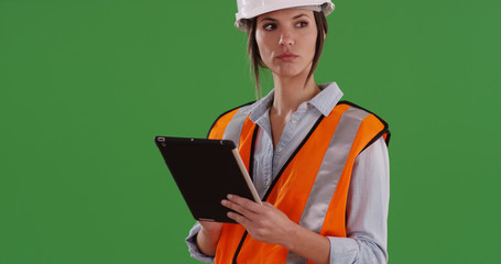 Female construction worker in orange vest and hard hat using pad on green screen