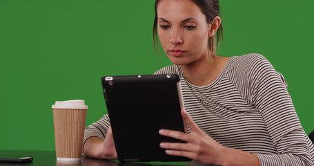 Millennial woman sitting at cafe table using tablet computer on green screen