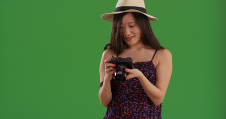 Young Asian female photographer with digital camera standing on green screen