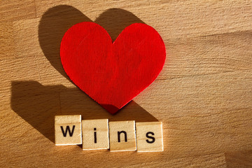 Creative background with scrabble letters and wooden heart shaped object, says love wins.