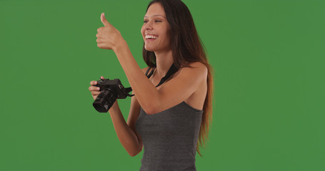Happy young female photographer giving thumbs up on green screen