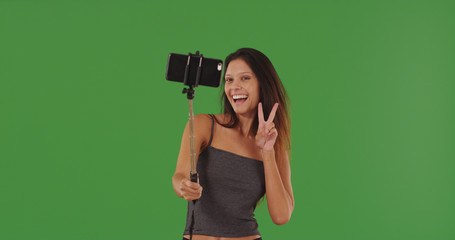 Caucasian girl using selfie-stick to take selfie with phone on green screen