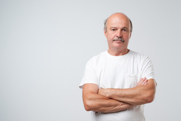 Charming handsome senior man in casual clothes keeping arms crossed and smiling