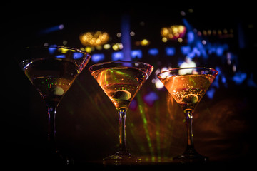 Several glasses of famous cocktail Martini, shot at a bar with dark toned foggy background and disco lights. Club drink concept
