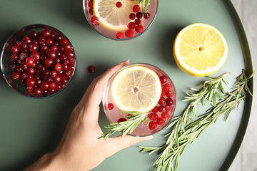 Woman holding glass of cranberry cocktail with rosemary on table, top view