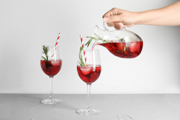 Woman pouring cranberry cocktail into glass with rosemary on table