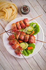 Chicken liver wrapped with bacon on skewers. Grilled liver kebabs with vegetables on white plate. overhead, vertical