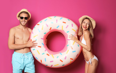 Happy young couple in beachwear with inflatable ring on color background