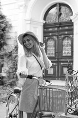 Naklejka premium Beautiful woman with bicycle near ornate door on street, black and white effect