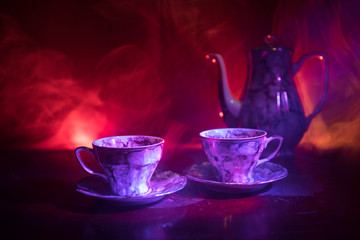 Food background tea and coffee theme. Old vintage ceramic tea or coffee pot with cups jug and sugar cup on dark background with lights and smoke. Silhouettes of ceramic tea pot and cup.