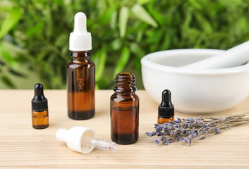 Bottles with natural herbal oil and lavender flowers on table against blurred background