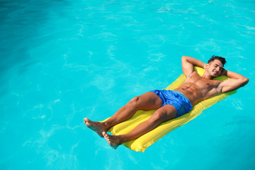 Young man with inflatable mattress in pool on sunny day