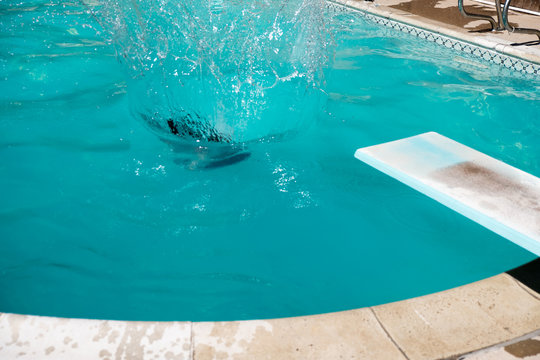 Woman Jumping Off Diving Board Doing A Cannon Ball Lands With Big Splash In The Swimming Pool. Girl Underwater, Jumps Off Diving Board Into An Outdoor Swimming Pool.