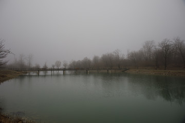 Amazing landscape of bridge reflect on surface water of lake, fog evaporate from pond make romantic scene or Beautiful bridge on lake with trees at fog.