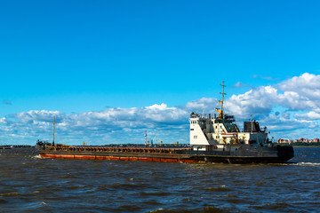Fototapeta premium A barge floating along the sea along the shore. The sea barge is transporting goods of the appropriate destination. The sea is calm. The weather is sunny.