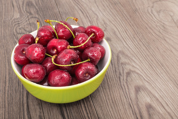 Group of sweet cherries in a green bowl. Prunus avium. Beautiful close-up of delicious fresh red cherry berries with water droplets. Pile of washed ripe juicy fruit on a brown wooden background.