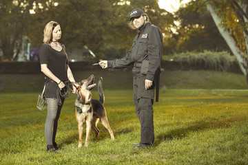 Policeman in uniform reproaching lady with german shepherd in city park