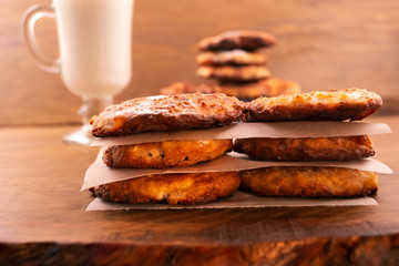 Cottage cheese cookies baked to a golden  brown, stacked on top of each other, glass of milk, wooden background.