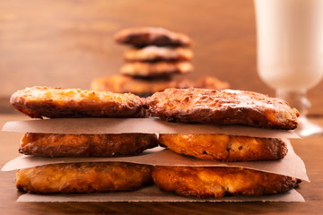 Homemade round biscuits with cottage cheese, stacked on top of each other on a wooden background, milk in a glass.