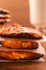 Cookies with a ruddy crust, stacked on top of each other in a column, a glass of milk, a wooden background, a vertical frame.