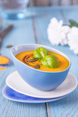 Homemade pumpkin cream soup with pumpkin seeds, pumpkin oil and turmeric on a blue background