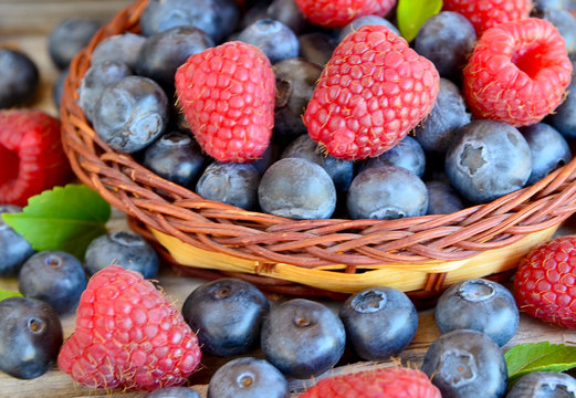 Freshly picked organic raspberries and blueberries in a basket on old wooden background.Blueberry and raspberry. Healthy eating,summer fruits or diet concept.Selective focus.