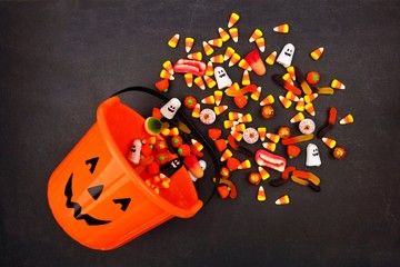 Halloween Jack o Lantern pail with spilling candy, above view on a dark background © Jenifoto