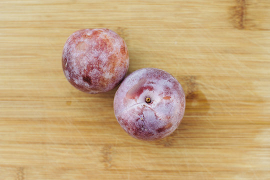Two honey punch pluot fruits sit on a wooden chopping board