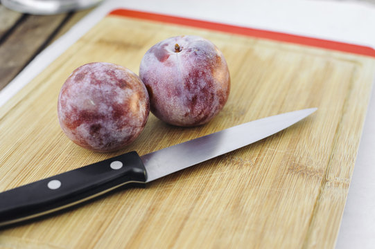A pair of Honey Punch Pluots on a chopping board with a knife