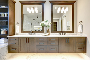 Master bathroom interior in luxury modern home with dark hardwood cabinets, white tub and glass...